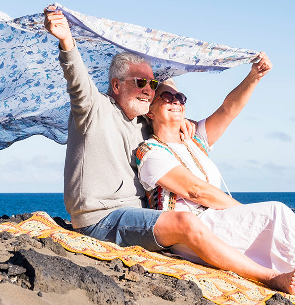 Happy Senior Couple Holding Blanket in Wind at Beach Retirement Made Simple Michigan