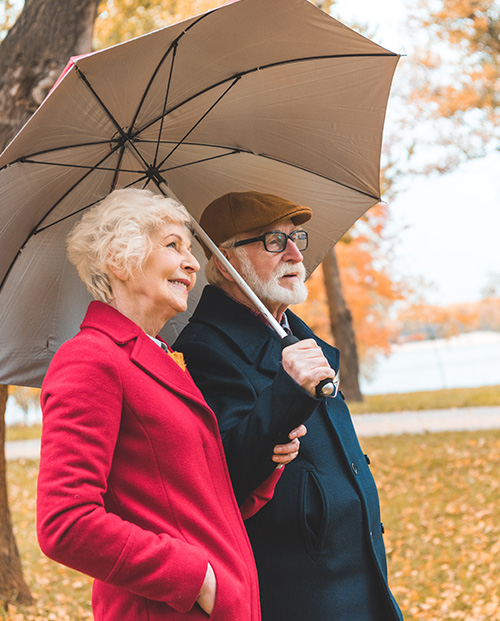 Senior Couple with Umbrella Walking in Park During Autumn What is an IUL Policy Michigan